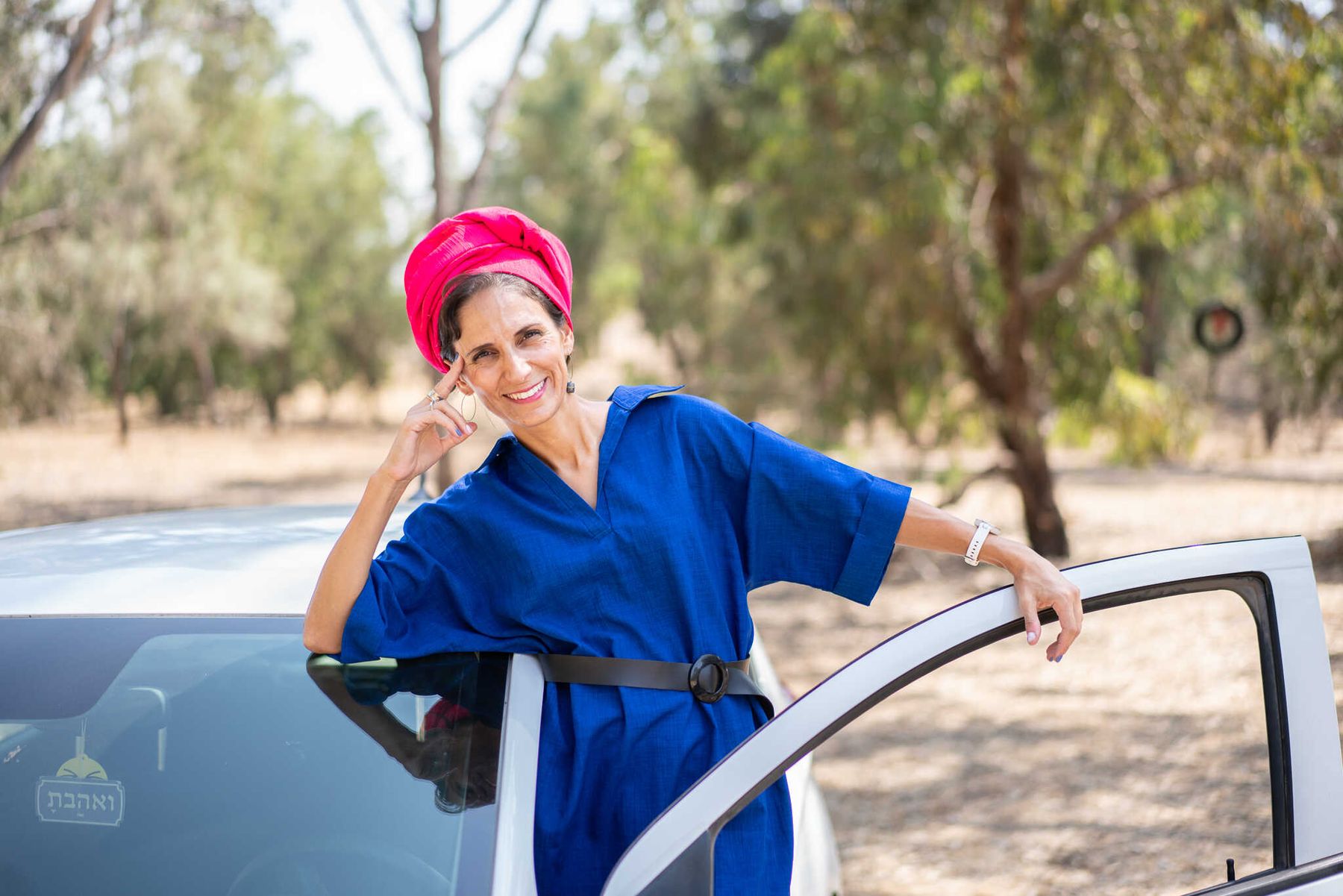 רוני נשענת על דלת הרכב הפתוחה ומחייכת